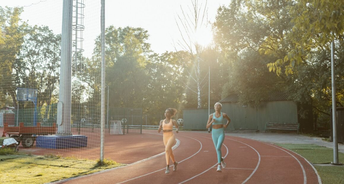 Two women jogging on an outdoor track, enjoying exercise and fitness in the morning sun.