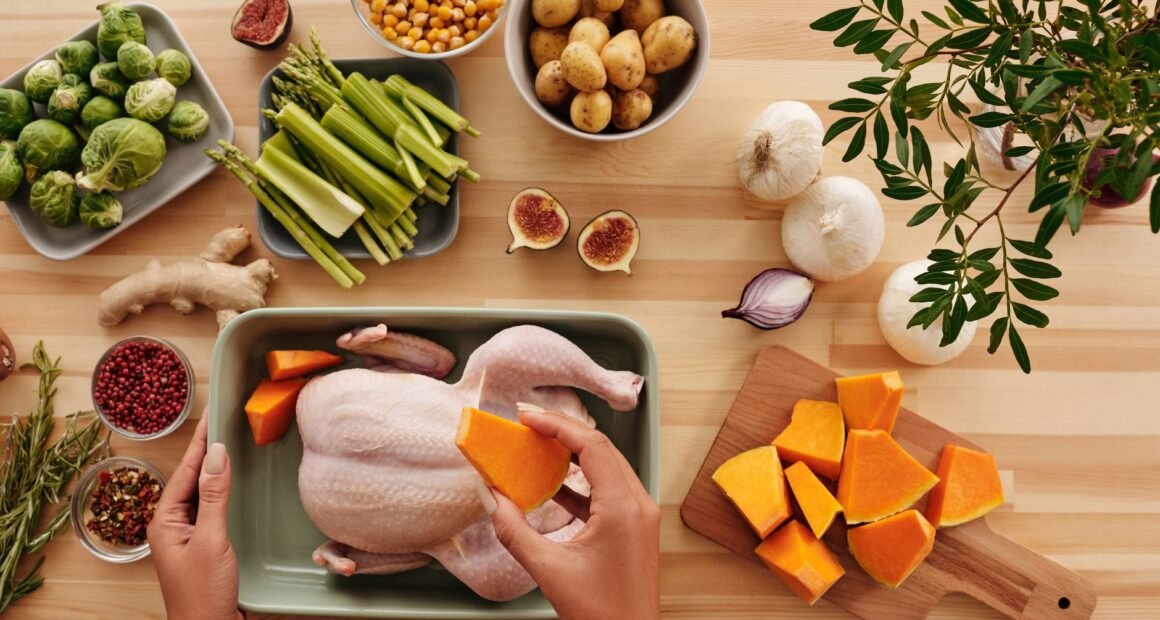 Hands preparing chicken with fresh vegetables on a wooden table.