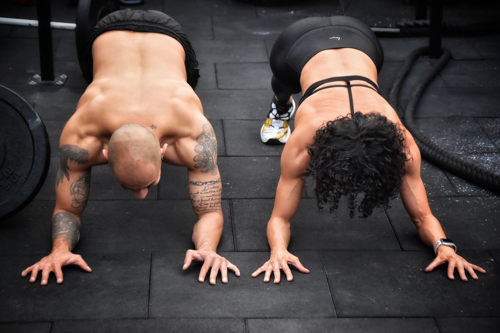 Homem e mulher fazendo exercício no chão, vistos de cima, sem rostos identificáveis.