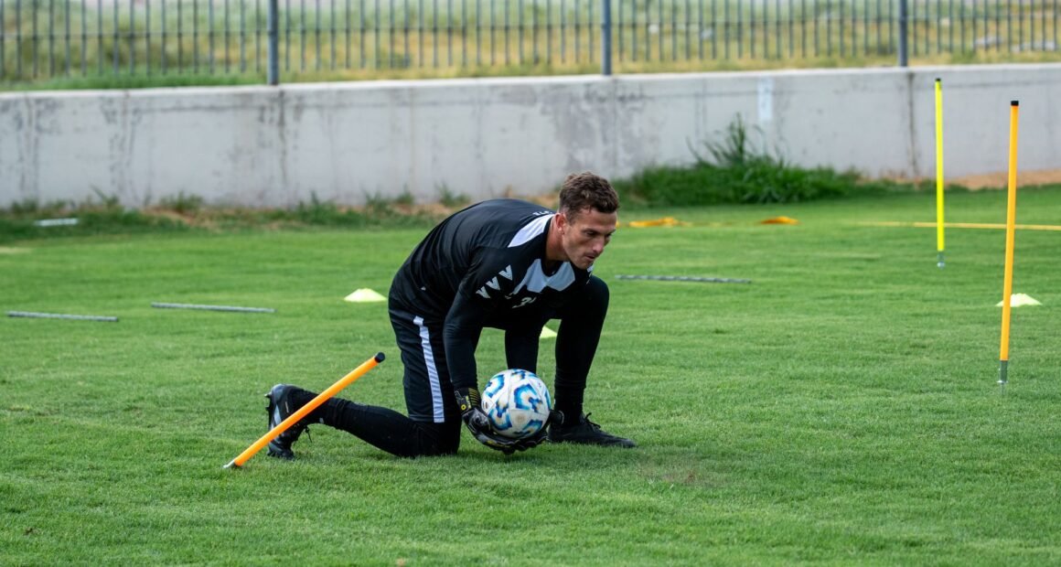 Athlete training on a grassy soccer field with a ball and training equipment.