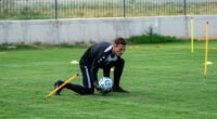 Athlete training on a grassy soccer field with a ball and training equipment.