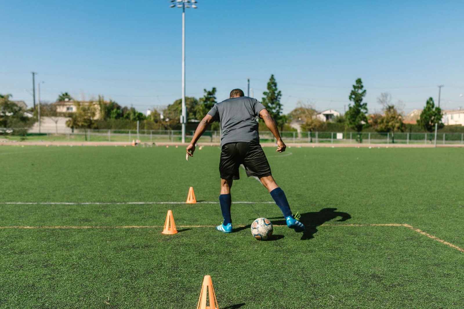 A soccer player practicing drills on a sunny day on an outdoor field.