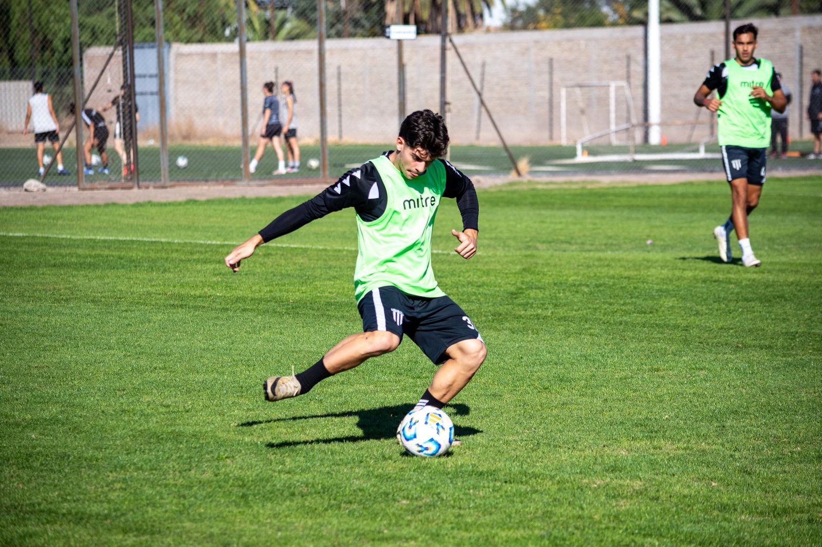 A young football player practicing with teammates on a sunny day outdoors.