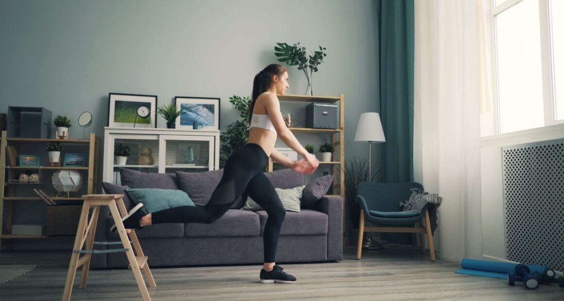 A woman in sportswear working out indoors using a chair for support, demonstrating leg exercises.