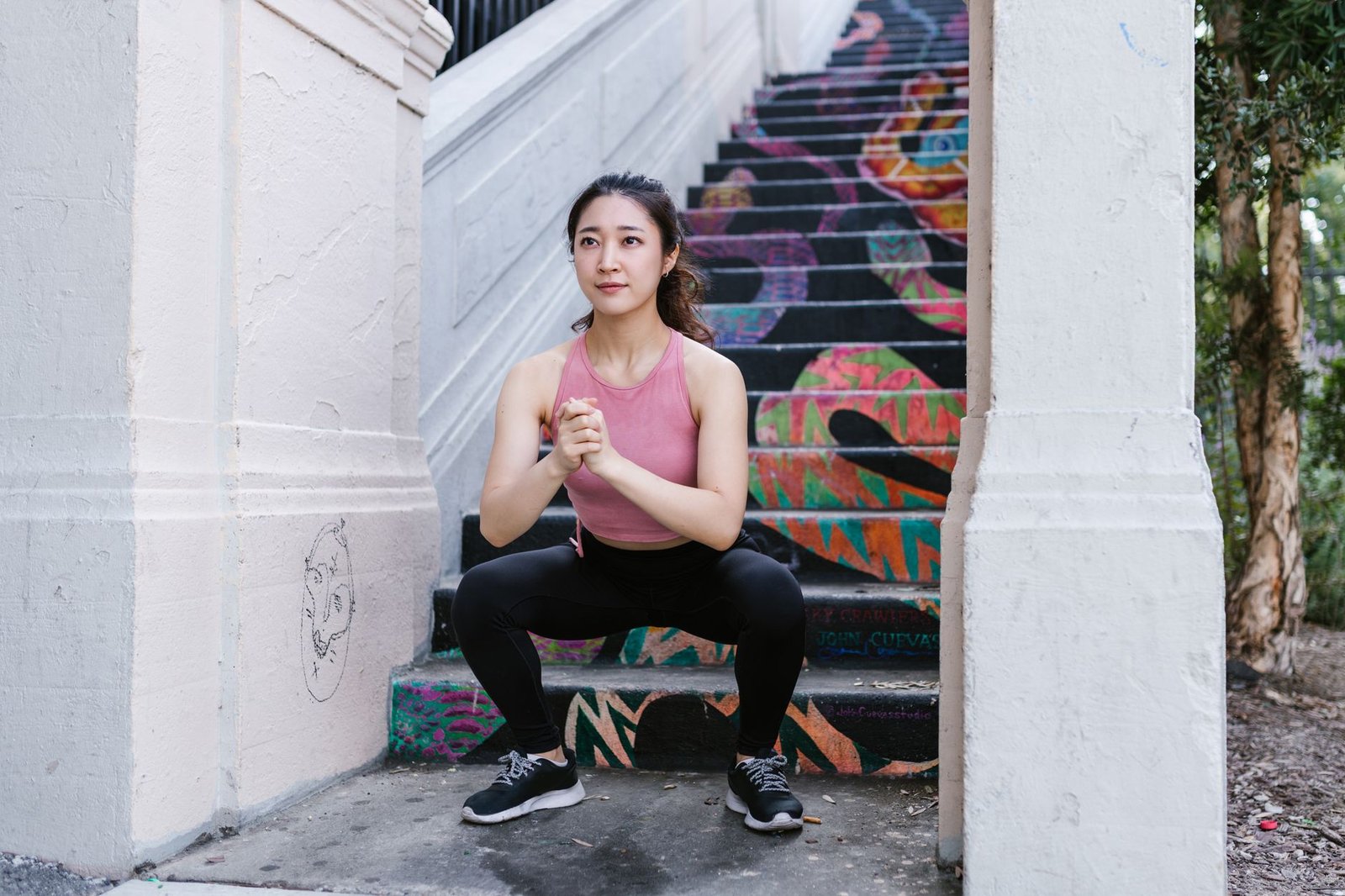 Asian woman squatting outdoors on a vibrant painted staircase, embracing active lifestyle.