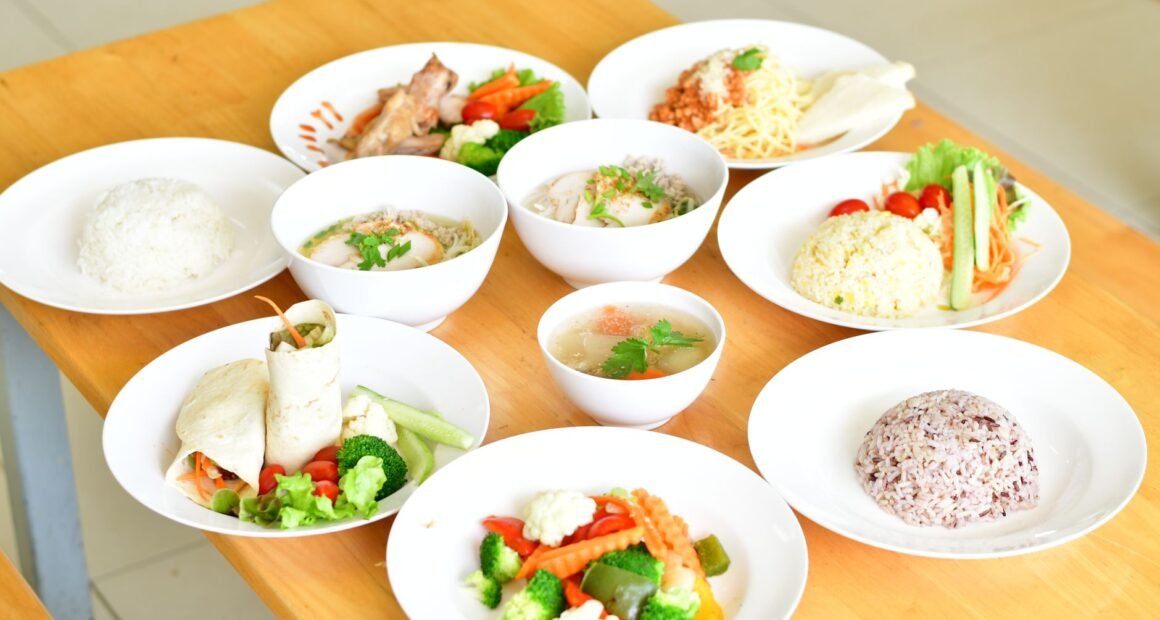 A variety of healthy dishes including rice, soup, and vegetables served on a wooden table.